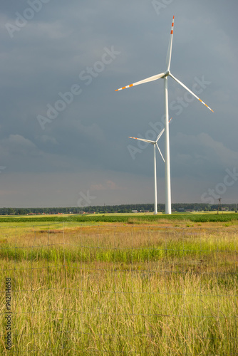 Obraz na płótnie Distant white wind turbines against a dramatic cloudy sky. Meadow in the foreground, taken late afternoon w salonie