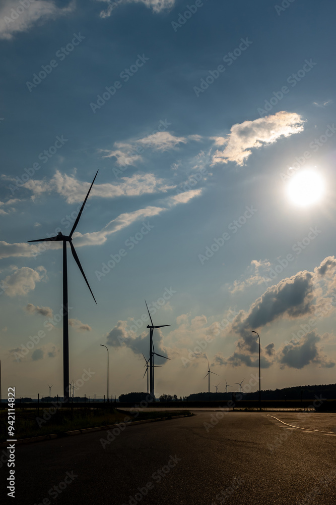 Wind turbines and high voltage electric pylon against blue sky. Sun shining behind the turbines
