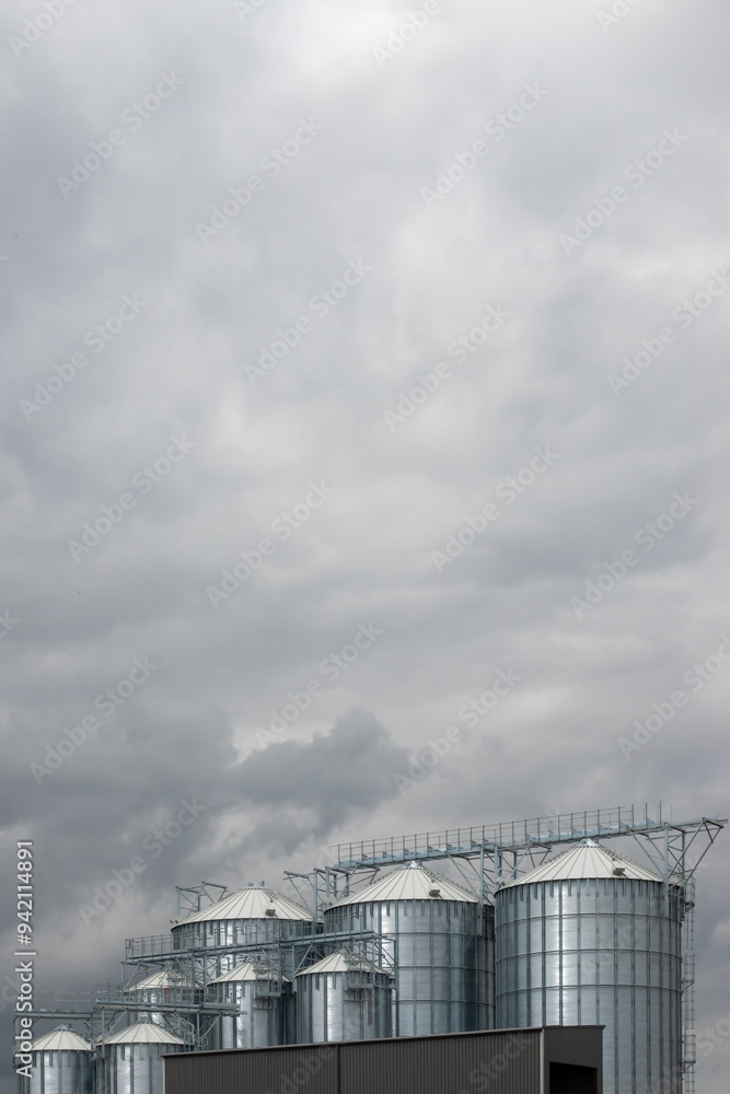 Steel grain silo against a dramatic, cloudy sky. Modern agriculture buildings photographed in the day .