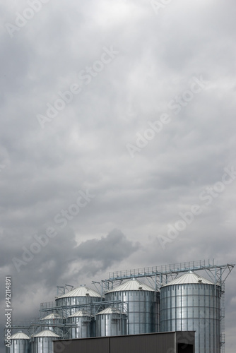 Obraz na płótnie Steel grain silo against a dramatic, cloudy sky. Modern agriculture buildings photographed in the day . w salonie