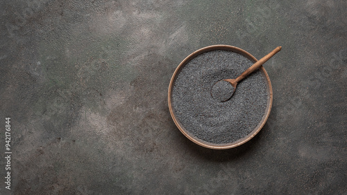 Poppy seeds in bowl with wooden spoon, dark grunge background. Top view, flat lay, copy space.