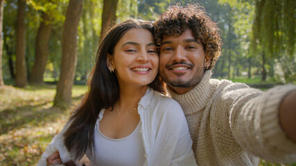 Carefree multiracial couple Arabic Indian male boyfriend happy Hispanic girlfriend woman making photo on mobile phone device outside in park man female laugh smile filming video cuddle honeymoon love