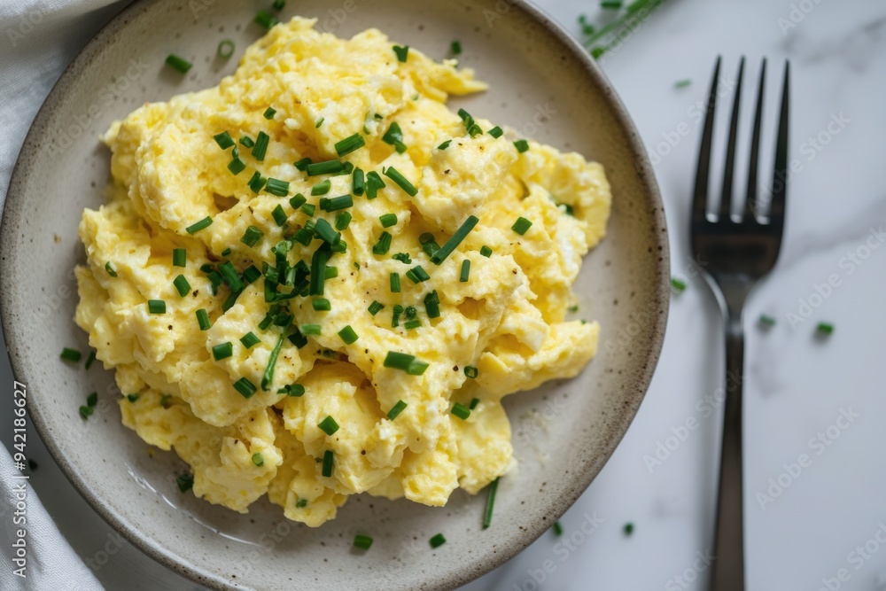 Overhead view of scrambled eggs on a plate, garnished with chopped chives, with a fork resting beside the plate Overhead view of scrambled eggs on a plate, garnished with chopped chives, with a fork resting beside the plate