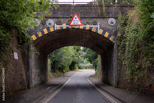 Low brick railway bridge over narrow road with height restriction sign