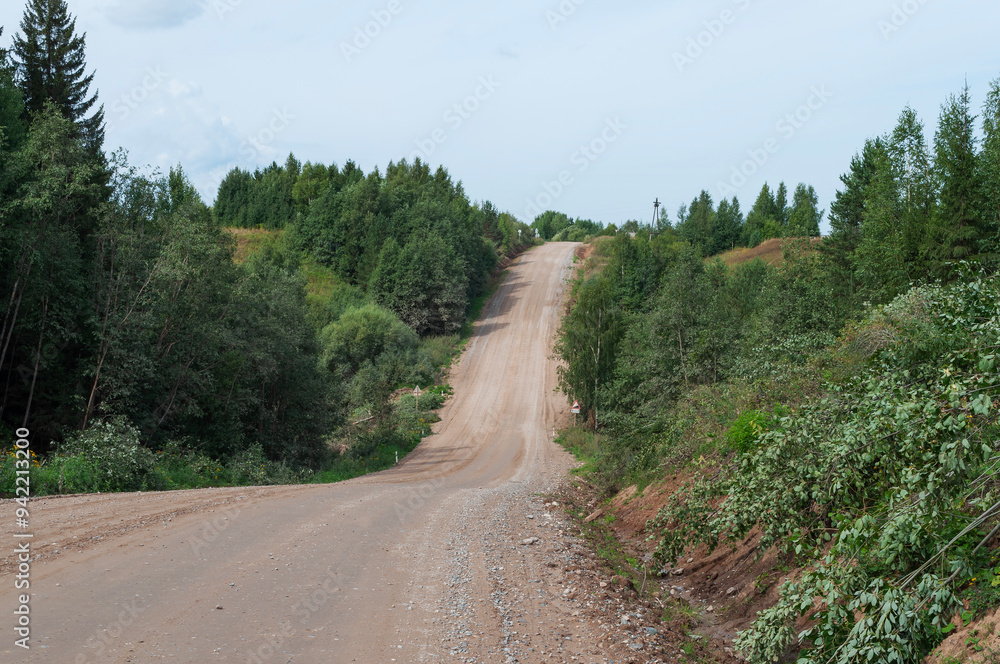 Fototapeta premium Country dirt road through forested hills, steep climbs and descents, clear summer day