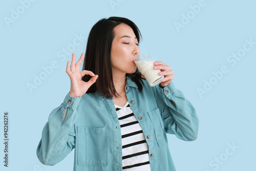 Beautiful Asian woman drinking milk and showing OK on light blue background photo