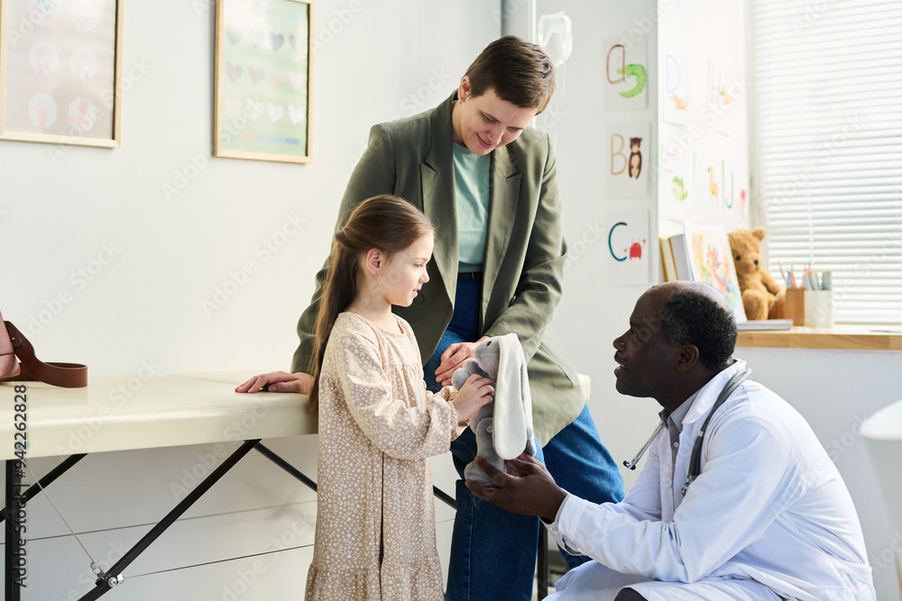 © pressmaster - Child receiving medical attention from doctor while parent watches Briefcase on table and medical equipment visible in background
