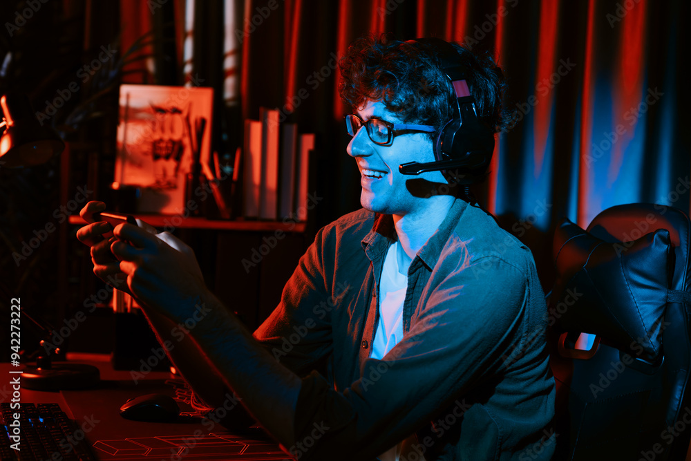 Fototapeta premium Smiling young gaming streamer team playing with Esport online on smartphone fighting wearing headphones at neon light room. Practising strategy plan to win competitors for next harder level. Gusher.