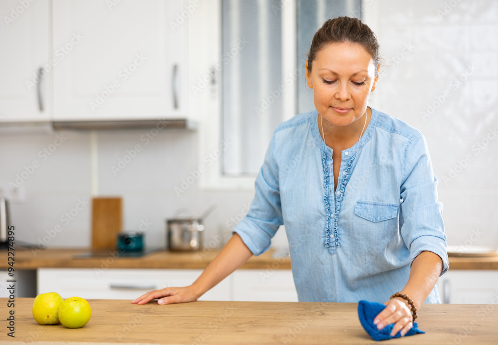 Fototapeta premium Positive woman cleaning kitchen countertop, keeping house clean during day