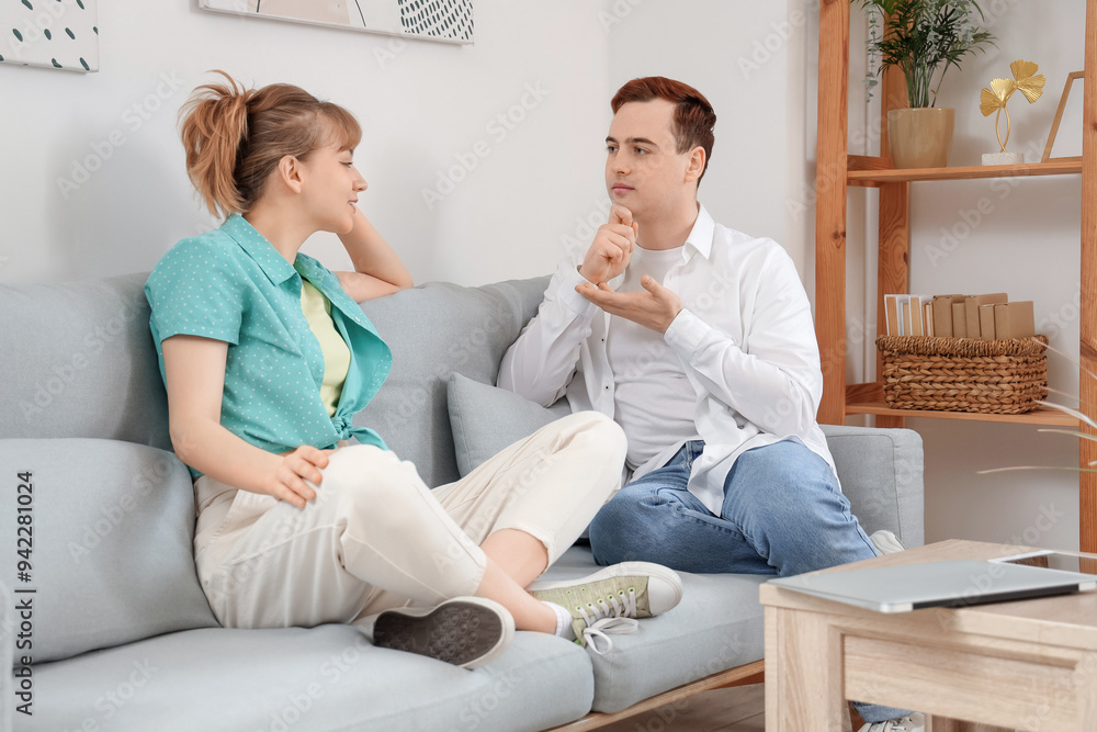 Young deaf mute couple using sign language on sofa at home Young deaf mute couple using sign language on sofa at home