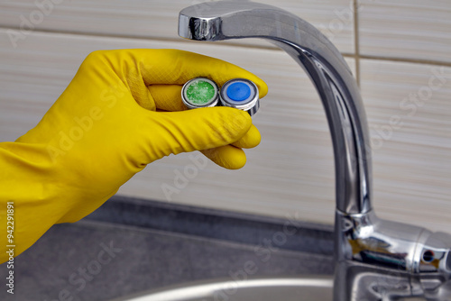 plumber's hand in yellow rubber gloves showing new and old clogged faucet aerator
