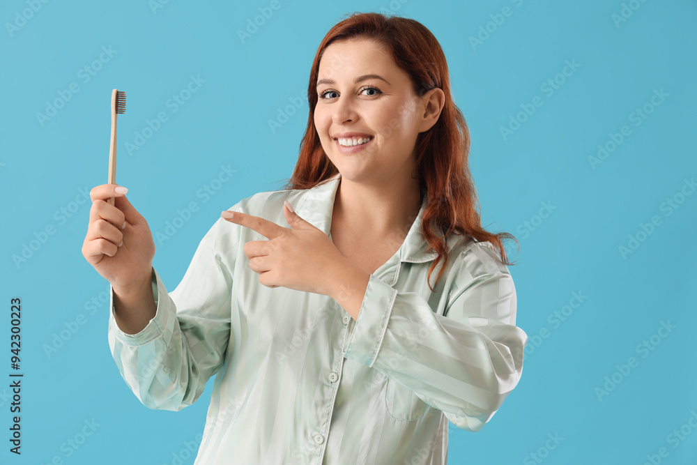 Young woman in pajamas pointing at toothbrush on blue background Young woman in pajamas pointing at toothbrush on blue background