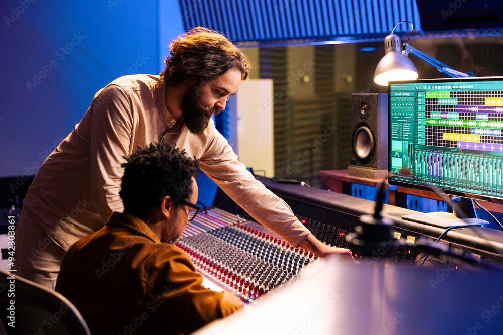 Diverse team of artist and audio engineer composing a hit song, working in professional music studio with technical gear. Musician with expert editing and recording music on mixing console board. Diverse team of artist and audio engineer composing a hit song, working in professional music studio with technical gear. Musician with expert editing and recording music on mixing console board.