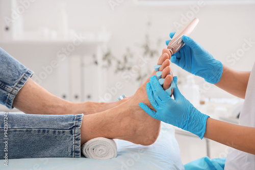 Beautician peeling feet of young man with toe separator on couch in spa salon, closeup