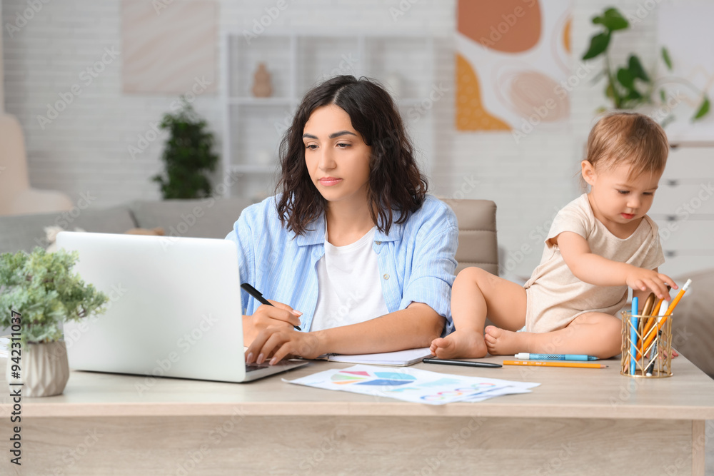 Cute little baby and young mother working with laptop while writing in notebook on maternity leave at home