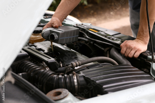 Male mechanic pouring car oil into engine outdoors, closeup