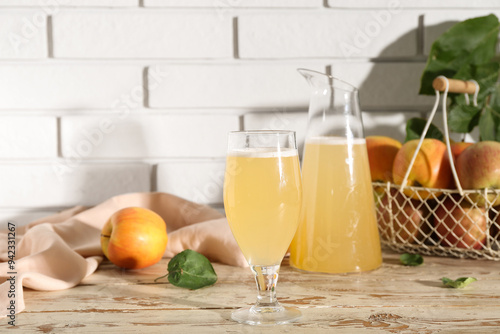 Glass and jug of fresh apple kvass on white wooden table photo