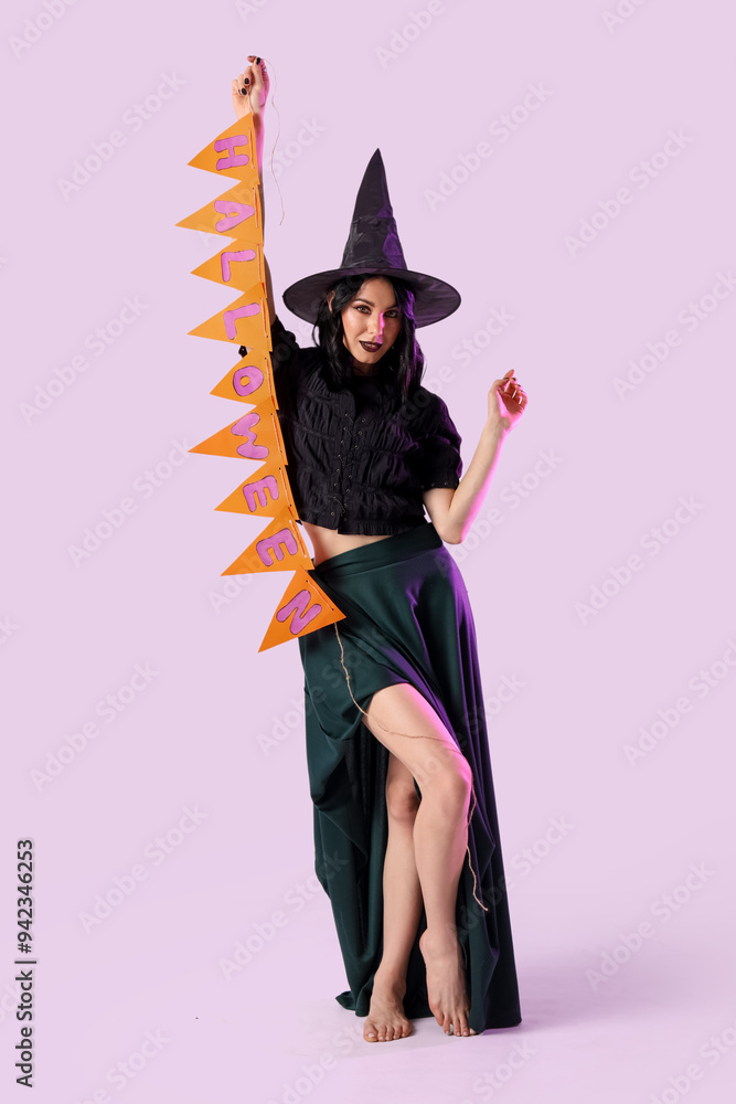 Beautiful young happy woman dressed as witch for Halloween with garland on lilac background Beautiful young happy woman dressed as witch for Halloween with garland on lilac background