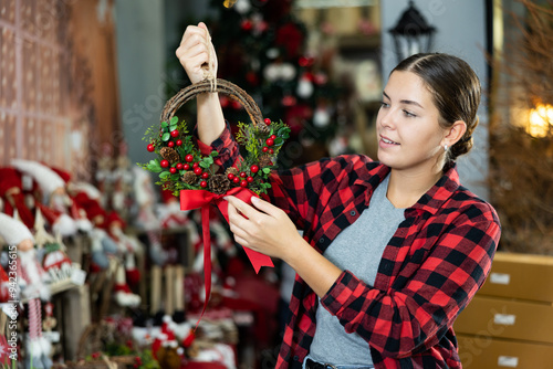 Happy female consumer choosing a farmhouse Christmas viburnum wreath at the decorated hall photo