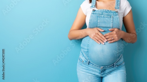Expectant Mother in Overalls Cradling Baby Bump Against Blue Background
