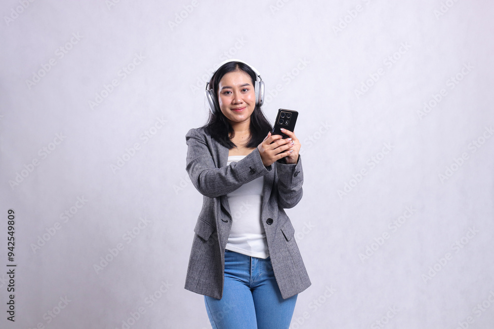 beautiful young office woman smile to camera wearing headphone headset and holding mobile phone streaming video wearing suit isolated on white background. education, entertainment, technology concept beautiful young office woman smile to camera wearing headphone headset and holding mobile phone streaming video wearing suit isolated on white background. education, entertainment, technology concept