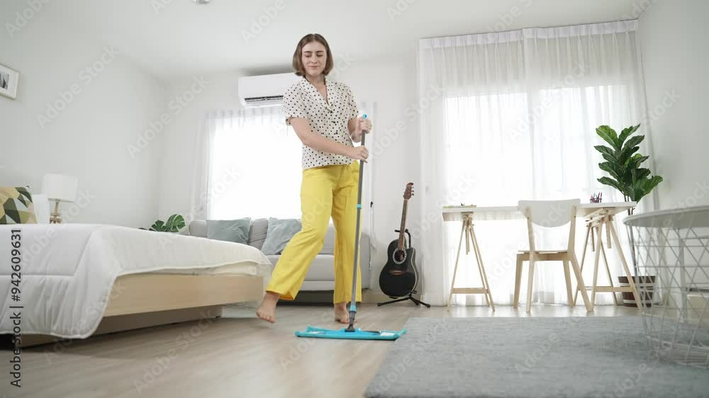 Caucasian housekeeper mopping the floor while dancing in lively mood at modern apartment. Happy energetic mother or cleaner enjoy cleaning the living room while moving to music. Lifestyle. Pedagogy. Caucasian housekeeper mopping the floor while dancing in lively mood at modern apartment. Happy energetic mother or cleaner enjoy cleaning the living room while moving to music. Lifestyle. Pedagogy.