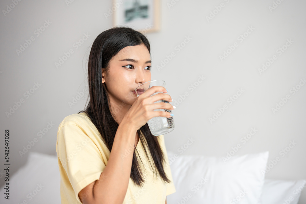 Asian attractive woman sit on bed, drink a glass of water in bedroom. Asian attractive woman sit on bed, drink a glass of water in bedroom.
