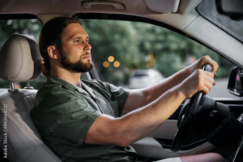Young man driving a car, focused and calm expression, seated in a modern vehicle Soft bokeh background with warm lighting effects Young man driving a car, focused and calm expression, seated in a modern vehicle Soft bokeh background with warm lighting effects
