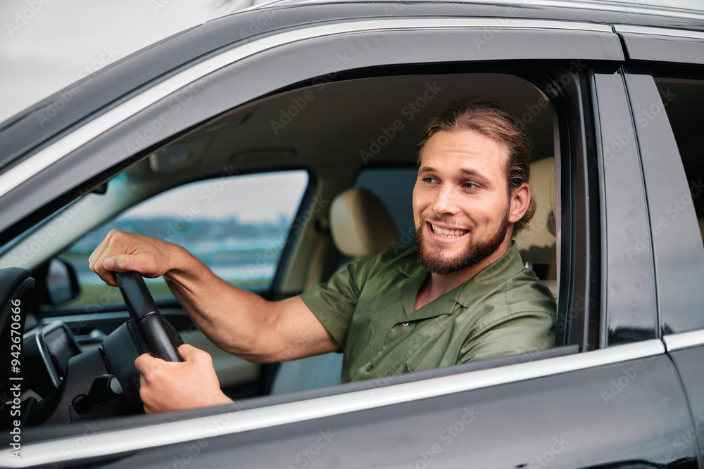 Smiling man driving a black car with confidence against an outdoor background Smiling man driving a black car with confidence against an outdoor background