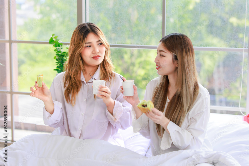 Two beautiful people happy Asian females drinking hot coffee or tea with bread or cake. Pretty woman laughing and talking relaxed funny on a white bed, Concept teenage or friends lifestyle at home. Two beautiful people happy Asian females drinking hot coffee or tea with bread or cake. Pretty woman laughing and talking relaxed funny on a white bed, Concept teenage or friends lifestyle at home.