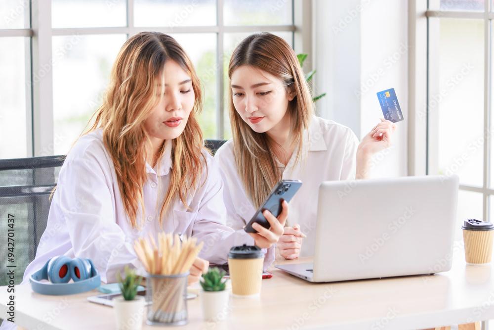 Two happy women, a beautiful Asian female using a computer laptop smiling while shopping online, and a credit card in the living room. Concept teenage or friends, time together lifestyle at home. Two happy women, a beautiful Asian female using a computer laptop smiling while shopping online, and a credit card in the living room. Concept teenage or friends, time together lifestyle at home.