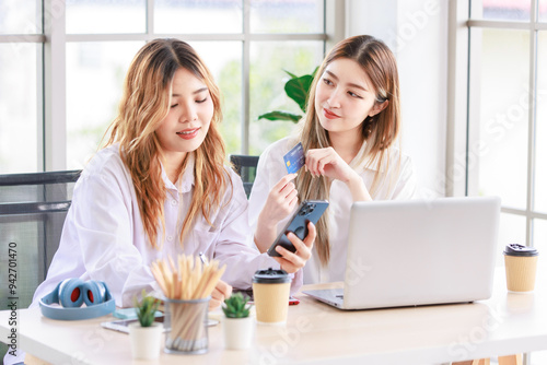 Two happy women, a beautiful Asian female using a computer laptop smiling while shopping online, and a credit card in the living room. Concept teenage or friends, time together lifestyle at home.