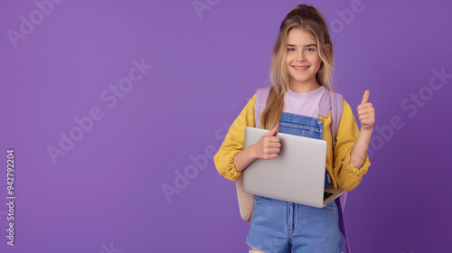 Portrait of a smiling young girl holding laptop computer, thumbs up gesture isolated over purple background.