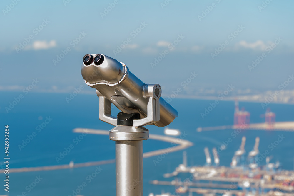 Close up of coin operated telescope is mounted on a sturdy base, pointing towards a distant scenic view in park. The binoculars are mounted an observation point for tourists to view distant landscapes Close up of coin operated telescope is mounted on a sturdy base, pointing towards a distant scenic view in park. The binoculars are mounted an observation point for tourists to view distant landscapes