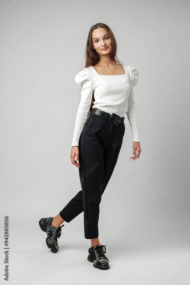 Young Woman in White Blouse and Black Pants Posing Against a White Background Young Woman in White Blouse and Black Pants Posing Against a White Background