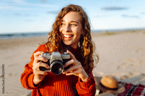 A young woman enjoying a sunny day at the beach while taking photos with her camera, captured in the warm light of the late afternoonю . Travel, blogging, technology concept. photo