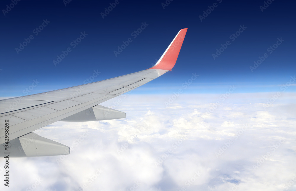 View from inside of plane through porthole. Wing of airplane at cloudscape. View from an aircraft window. Plane's wing with white clouds and blue sky View from inside of plane through porthole. Wing of airplane at cloudscape. View from an aircraft window. Plane's wing with white clouds and blue sky