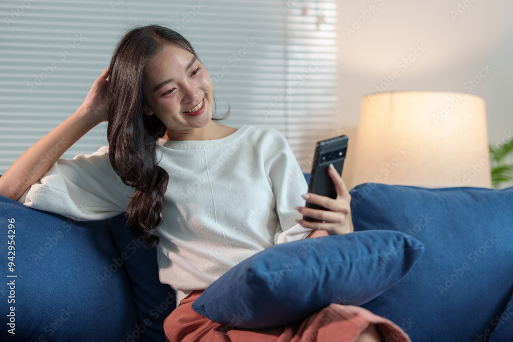 Happy and relaxed Asian woman sitting on sofa on weekend using smartphone to communicate, talk, text, chat online, watch wireless internet on device. Shopping online from your home office. Happy and relaxed Asian woman sitting on sofa on weekend using smartphone to communicate, talk, text, chat online, watch wireless internet on device. Shopping online from your home office.