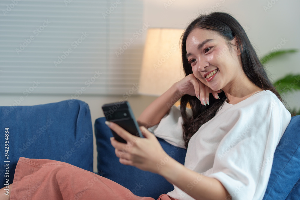 Happy and relaxed Asian woman sitting on sofa on weekend using smartphone to communicate, talk, text, chat online, watch wireless internet on device. Shopping online from your home office. Happy and relaxed Asian woman sitting on sofa on weekend using smartphone to communicate, talk, text, chat online, watch wireless internet on device. Shopping online from your home office.