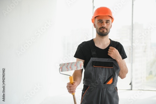 Portrait of man holding paint roller while painting white wall and making renovation photo