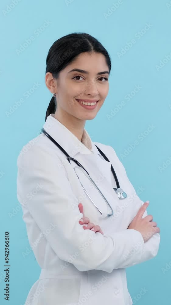 Portrait of a female happy and cheerful Caucasian young doctor or nurse, standing with crossed arms on blue background. Vertical video. Portrait of a female happy and cheerful Caucasian young doctor or nurse, standing with crossed arms on blue background. Vertical video.