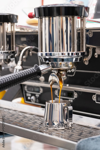 Close-up of espresso extraction process from a coffee machine, capturing the rich flow of coffee into a shiny cup.