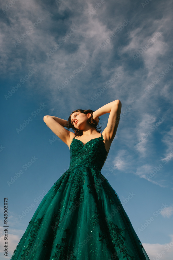 Young woman in elegant emerald prom dress under cloudy sky Young woman in elegant emerald prom dress under cloudy sky