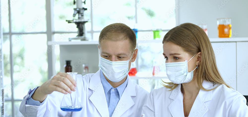 A team of two scientists in lab coats and masks work in a laboratory. A team of two scientists in lab coats and masks work in a laboratory.