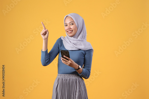 Canvas-taulu happy asian indonesian muslim woman holding smart phone with pointing finger ges