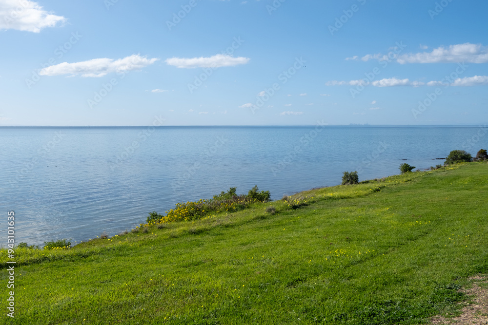 The background texture of a green grass lawn against the smooth, calm ocean, clear blue sky. This coastal scenery at Portarlington overlooks Port Phillip Bay on the Bellarine Peninsula. The background texture of a green grass lawn against the smooth, calm ocean, clear blue sky. This coastal scenery at Portarlington overlooks Port Phillip Bay on the Bellarine Peninsula.
