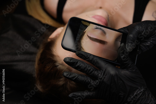 After completing the permanent makeup procedure, the master takes a photo of the client's eyebrows on her phone and looks at the result afterward. Permanent eyebrow makeup, eyebrow tattooing