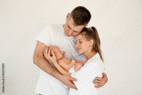 young parents with a newborn baby hug and kiss, happy mom and dad admiring the baby at home on the bed, a happy family caring for a small child, a place for text