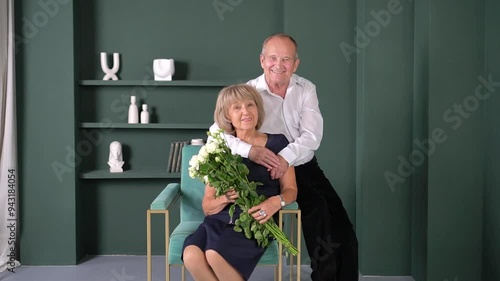 An elderly man tenderly kisses an elderly lady on the cheek and they are embarrassed. Flowers in their hands, happy wedding anniversary.