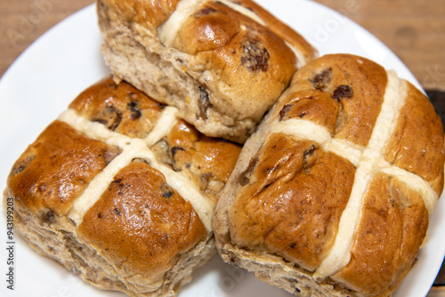 A delicious plate of three hot cross buns on a kitchen table